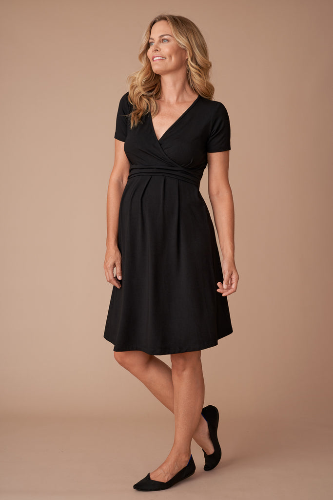 Pregnant woman wears Petit from Poa’s extremely versatile little black maternity dress. Finishing at the knee, with elegant short sleeves, it’s a stylish option for any smart casual occasion.